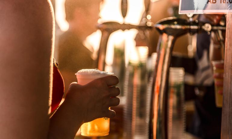 Person mit Bier an der Bar bei Sonnenuntergang.