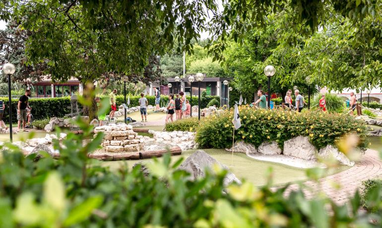 Mensen spelen minigolf in een zonnig, groen park.