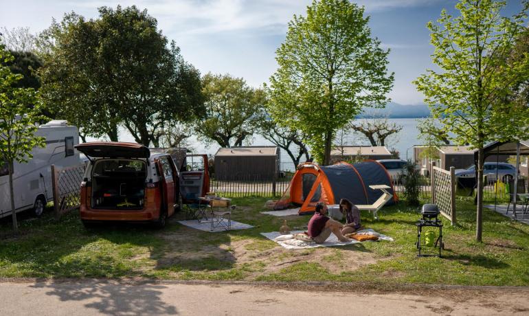 Camping med telt, varevogn, grill og to afslappende personer.