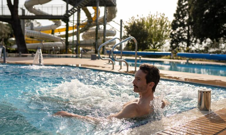 Mann entspannt sich im Pool mit Wasserrutschen im Hintergrund.