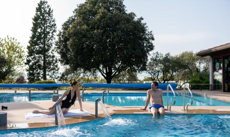 Due persone rilassate a bordo piscina con alberi sullo sfondo.