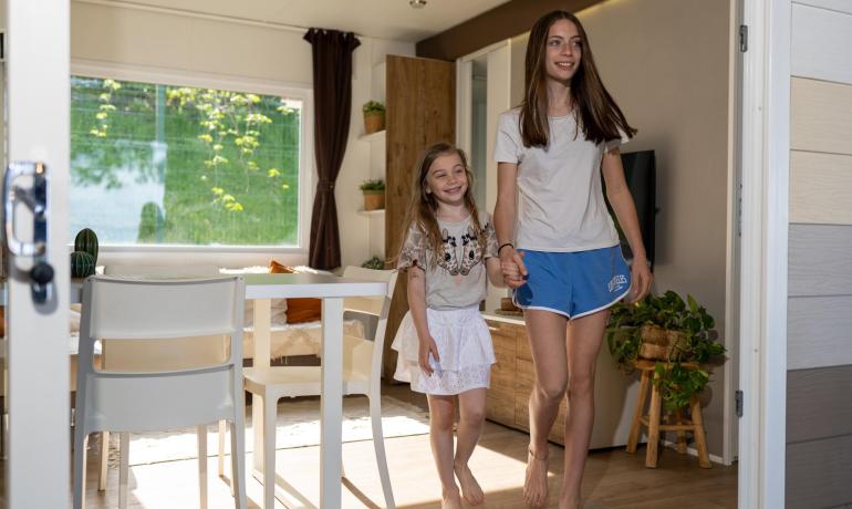 Twee lachende meisjes betreden een lichte, moderne kamer.
