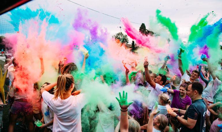 Persone gioiose lanciano polveri colorate in aria durante una festa all'aperto.