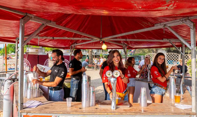 Sommerfest mit Lächeln und Fassbier unter einem roten Zelt.