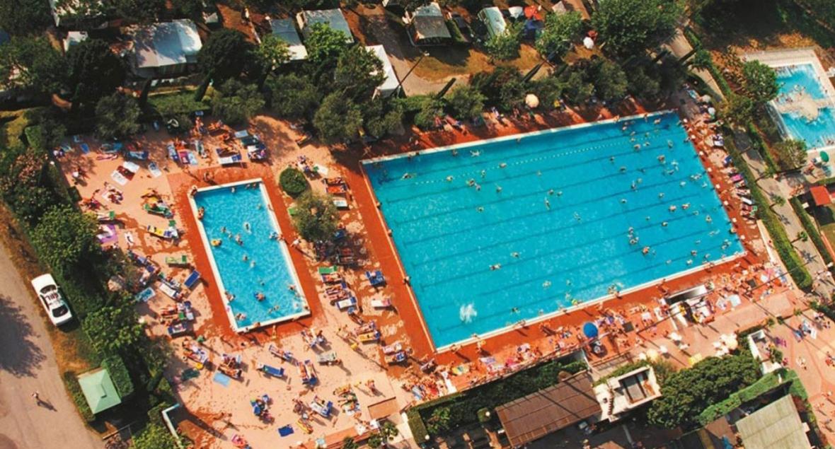 Luchtfoto van een druk zwembad met mensen die zwemmen en zonnebaden.