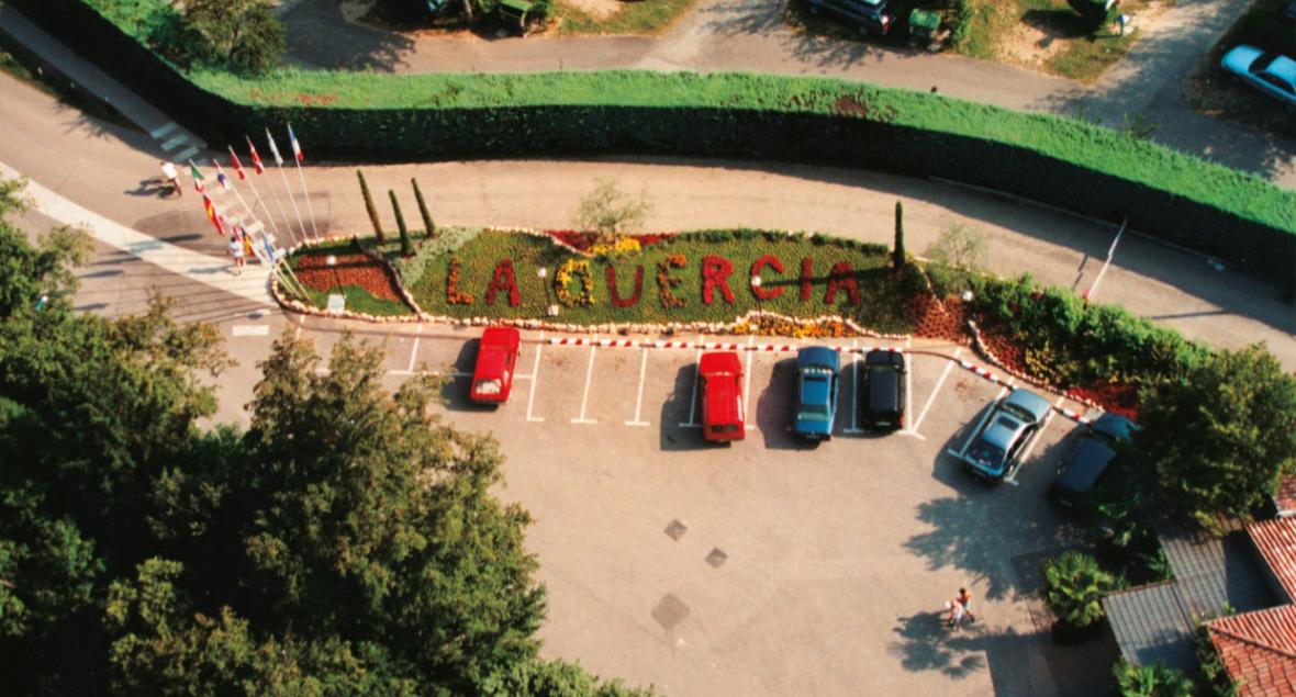 Luchtfoto van een parkeerplaats met 'LA QUERCIA' in bloemen geschreven.