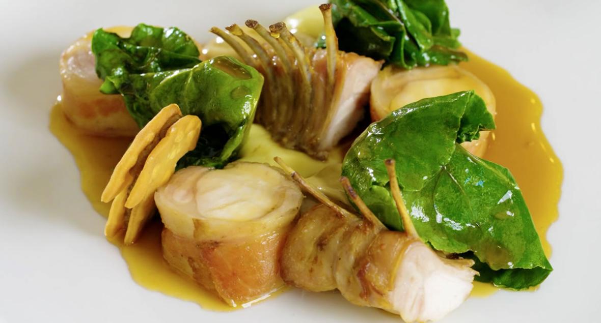 Gourmetret med kød, grønne blade og gul sauce.