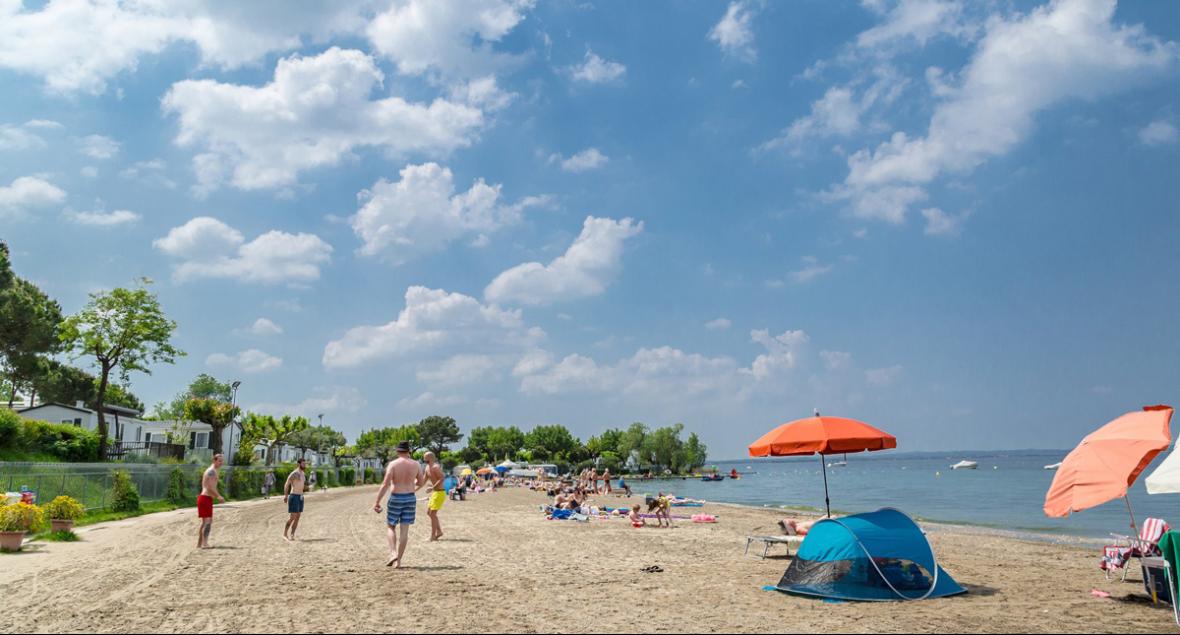 Sonniger Strand, blauer Himmel, bunte Sonnenschirme, entspannte Menschen, ruhiges Meer.