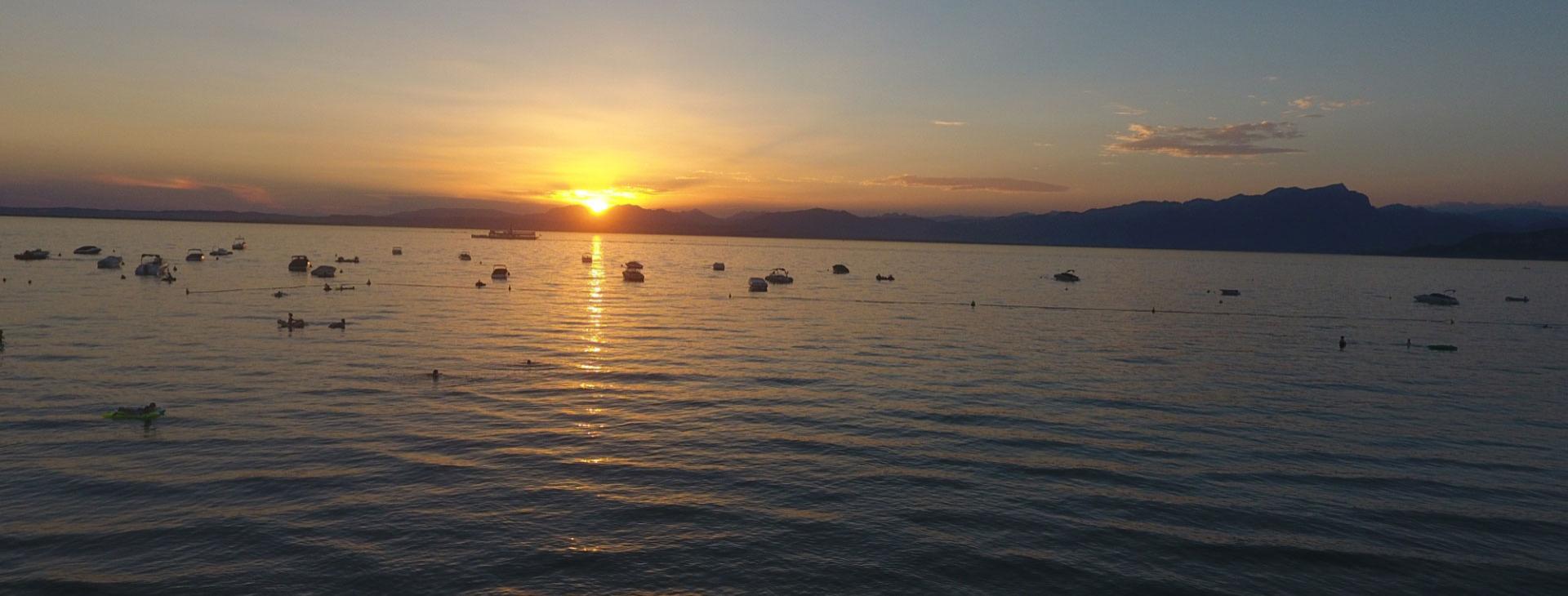 Sunset over the lake with boats and mountains in the distance.