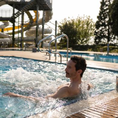 Pool med vandstråler og fitnesscenter i baggrunden.