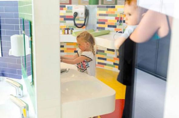 Bambina si lava le mani in bagno colorato, adulto con bambino osserva.