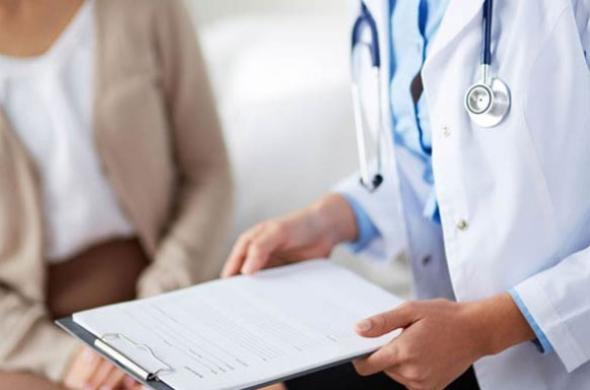 Medico con stetoscopio consulta una cartella clinica accanto a un paziente.