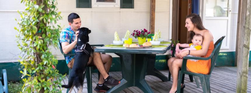 Family sitting at an outdoor table with a dog and a baby.